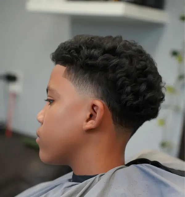 A curly top with a skin fade, in profile, cut by Leandro Herrera